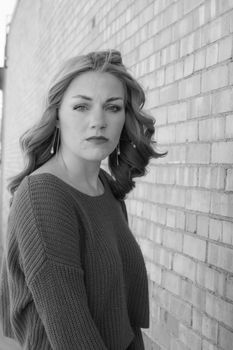 Elegant black and white portrait of a young woman in knitwear posing against a brick wall.