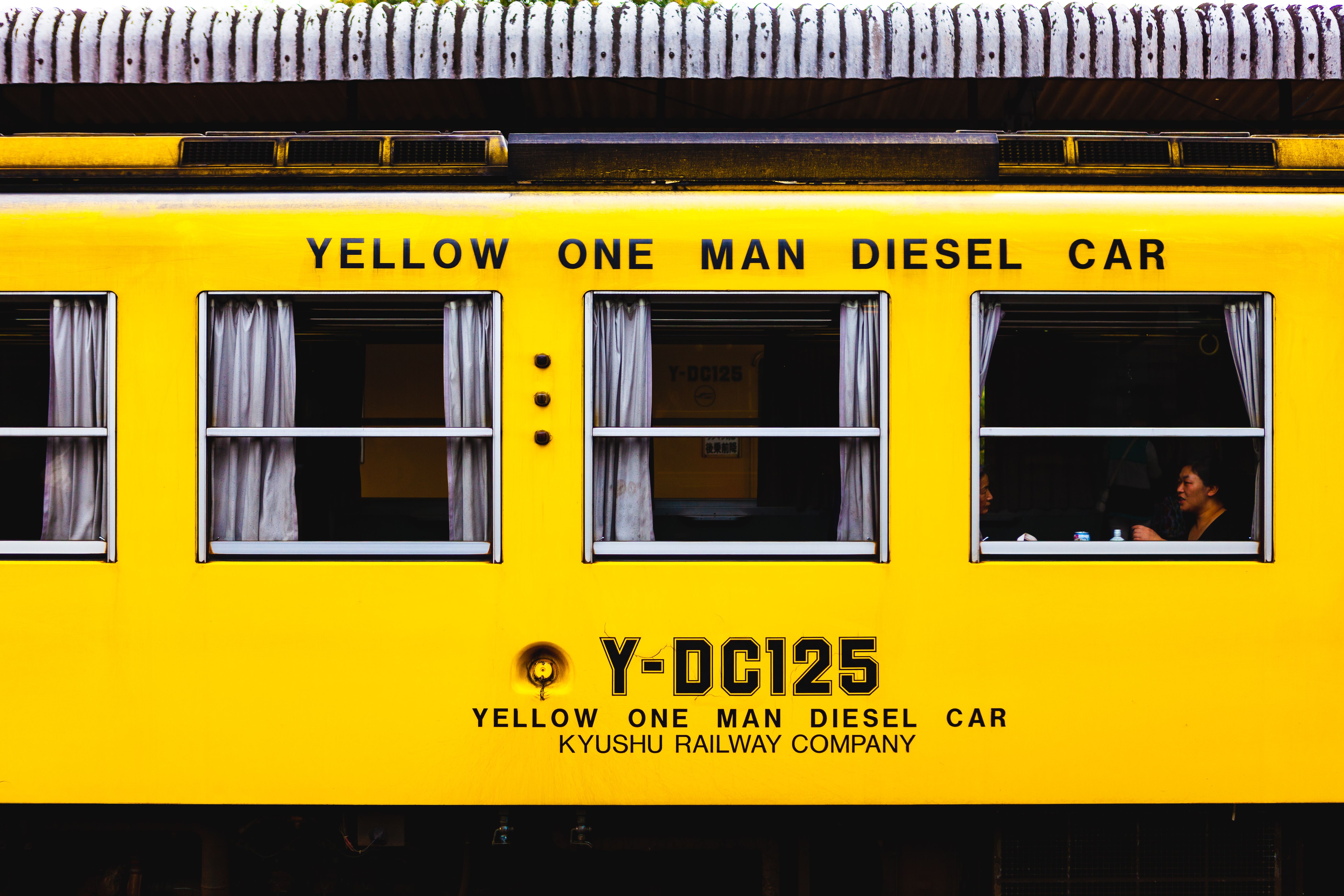 Close-up of a yellow diesel train in Kyushu, Japan with passengers visible through windows.