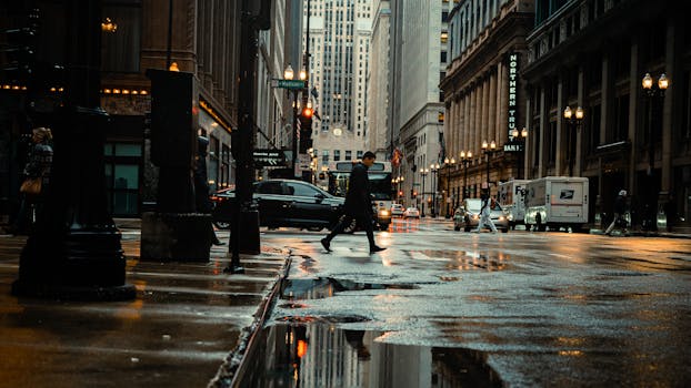 Pedestrian crossing a wet street in downtown Chicago, reflecting urban life and architecture.