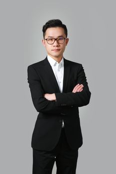 Professional portrait of a man in a black suit crossing arms against a gray background.