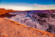 日落时分，冰岛古尔福斯瀑布的壮丽景色展现了冰层与崎岖的悬崖