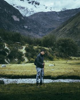 Man hiking through scenic mountain landscape with stream and grassy meadow.