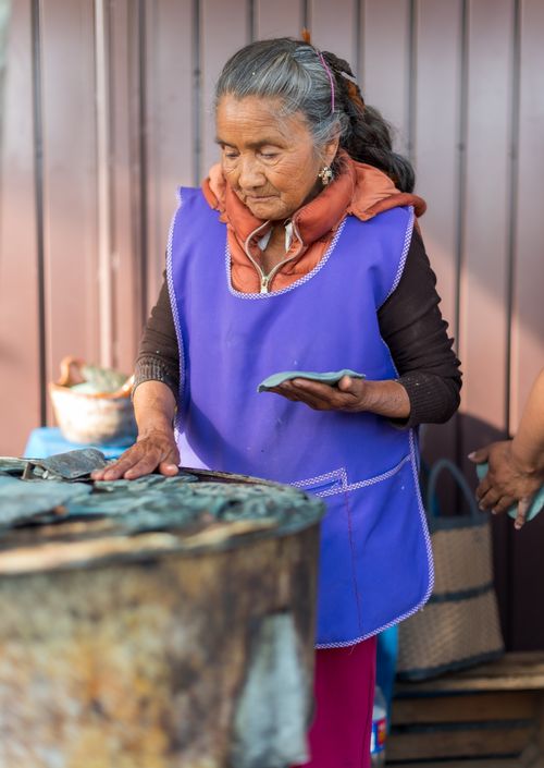 Free Senior woman cooking flatbreads outdoors in traditional setting, wearing apron Stock Photo