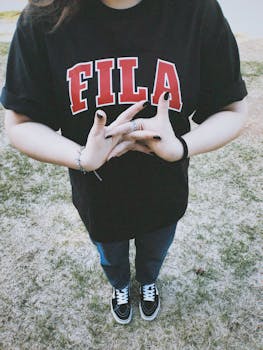 Person in a black Fila t-shirt standing on grass, hands clasped outdoors.