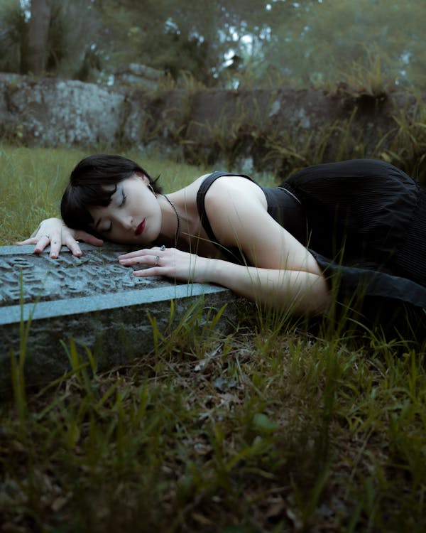 Woman in Black Dress Lying Down on Gravestone