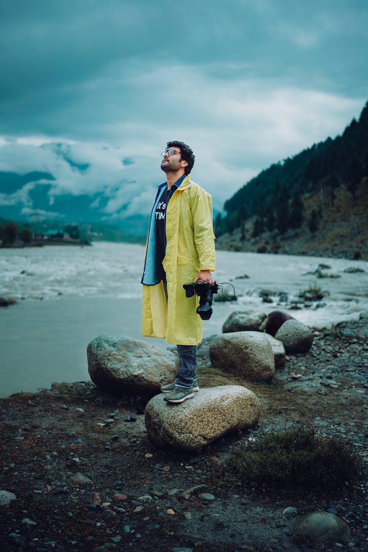 Man In Raincoat And With Camera Standing Near River