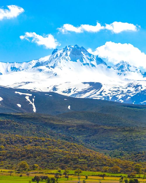 Free A breathtaking aerial view of snow-capped Mount Erciyes towering over lush green landscapes in Kayseri, Türkiye. Stock Photo