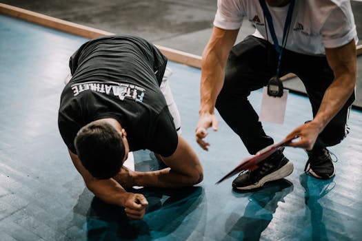 An athlete being assisted by a coach during an indoor training session on a blue floor.