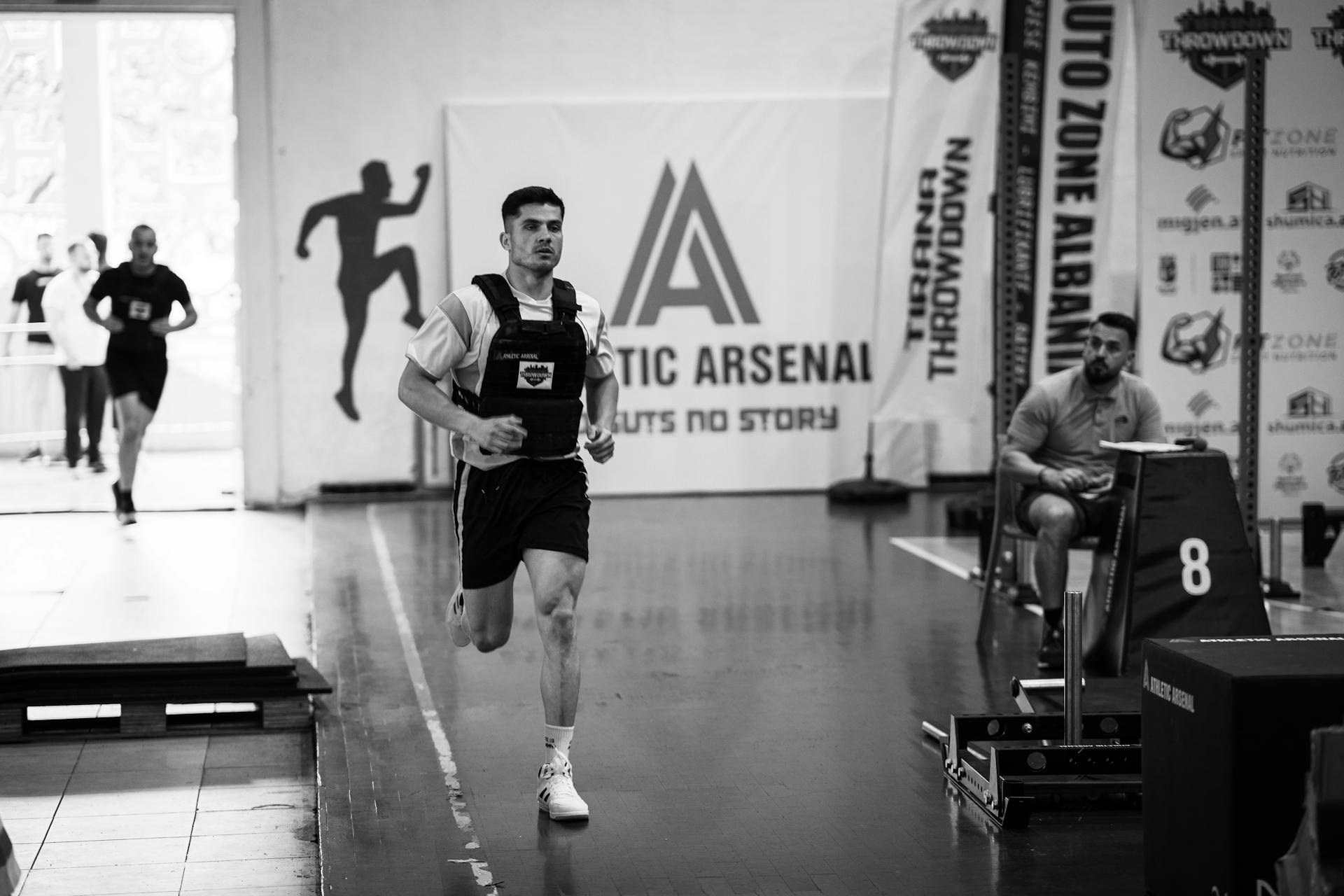 Male athlete running indoors during a competitive sports event with fitness branding.