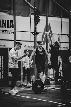 Group of adults engaging in weight lifting at a modern gym. Black and white photograph adds a classic touch.