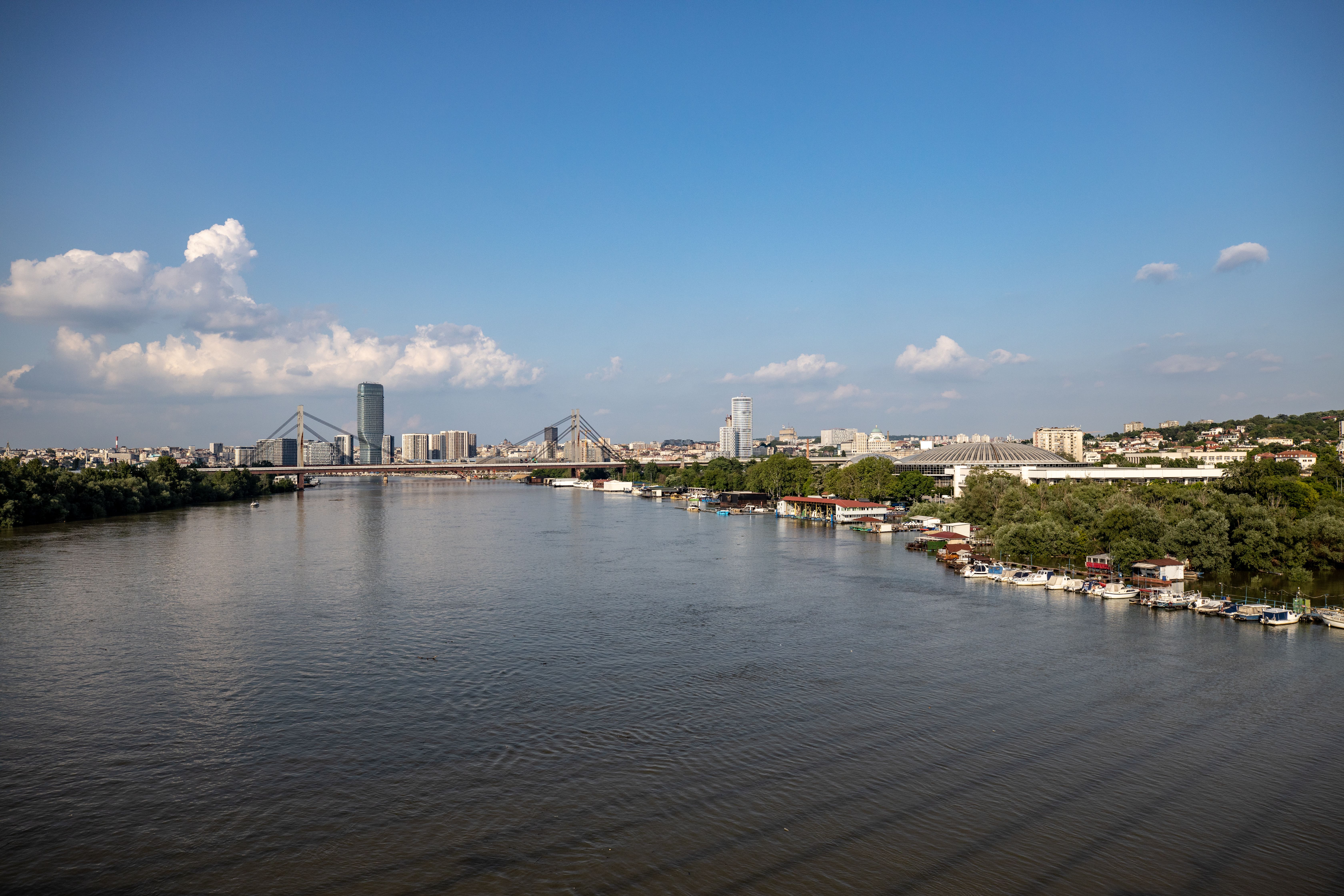 Aerial view of Belgrade with its iconic bridge and city skyline along the river under a clear blue sky.