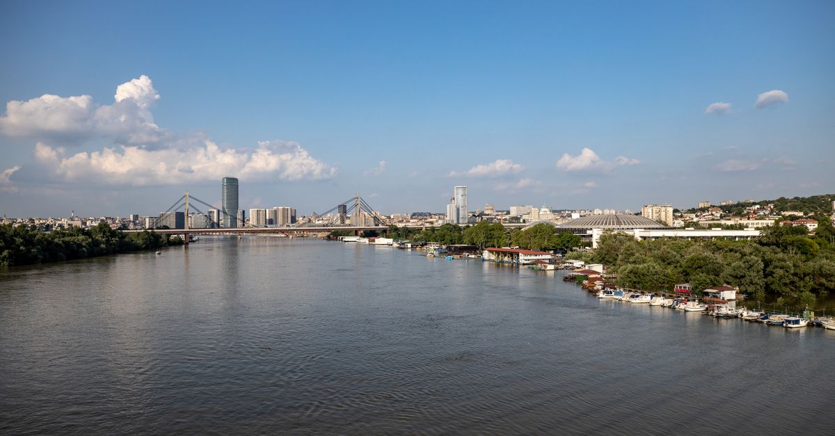 Aerial view of Belgrade with its iconic bridge and city skyline along the river under a clear blue sky.