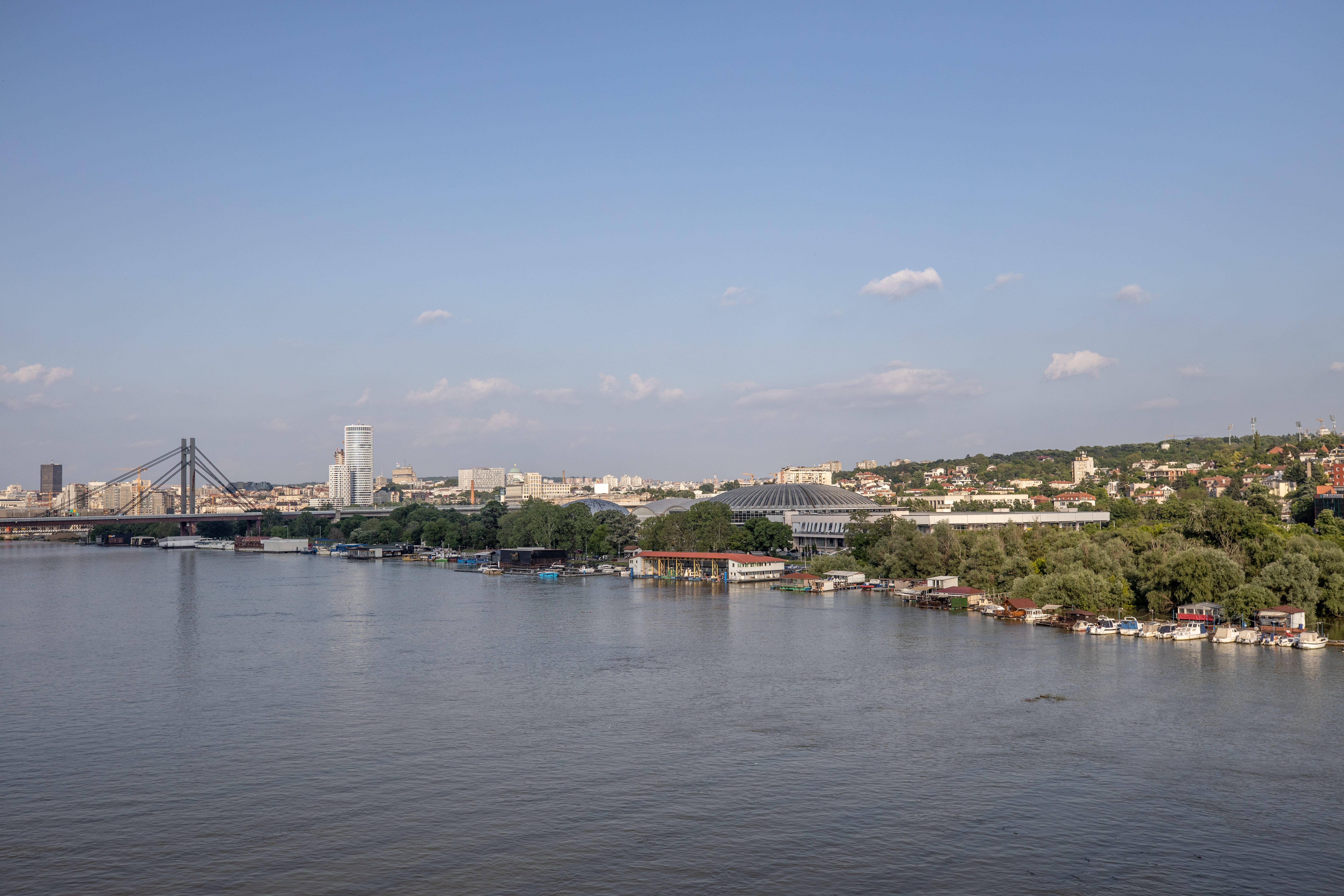 Scenic aerial view of a city skyline with a prominent river and bridge under a clear blue sky.