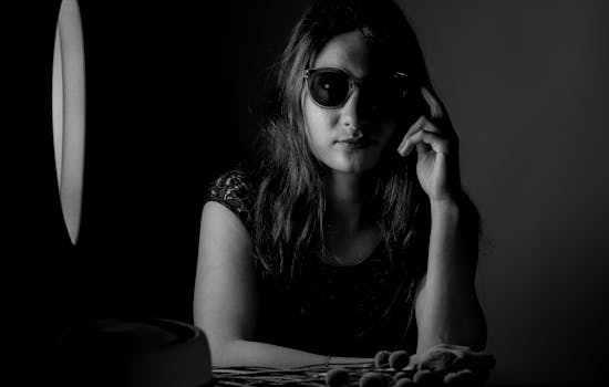 Moody black and white portrait of a woman in sunglasses with dramatic shadow lighting.