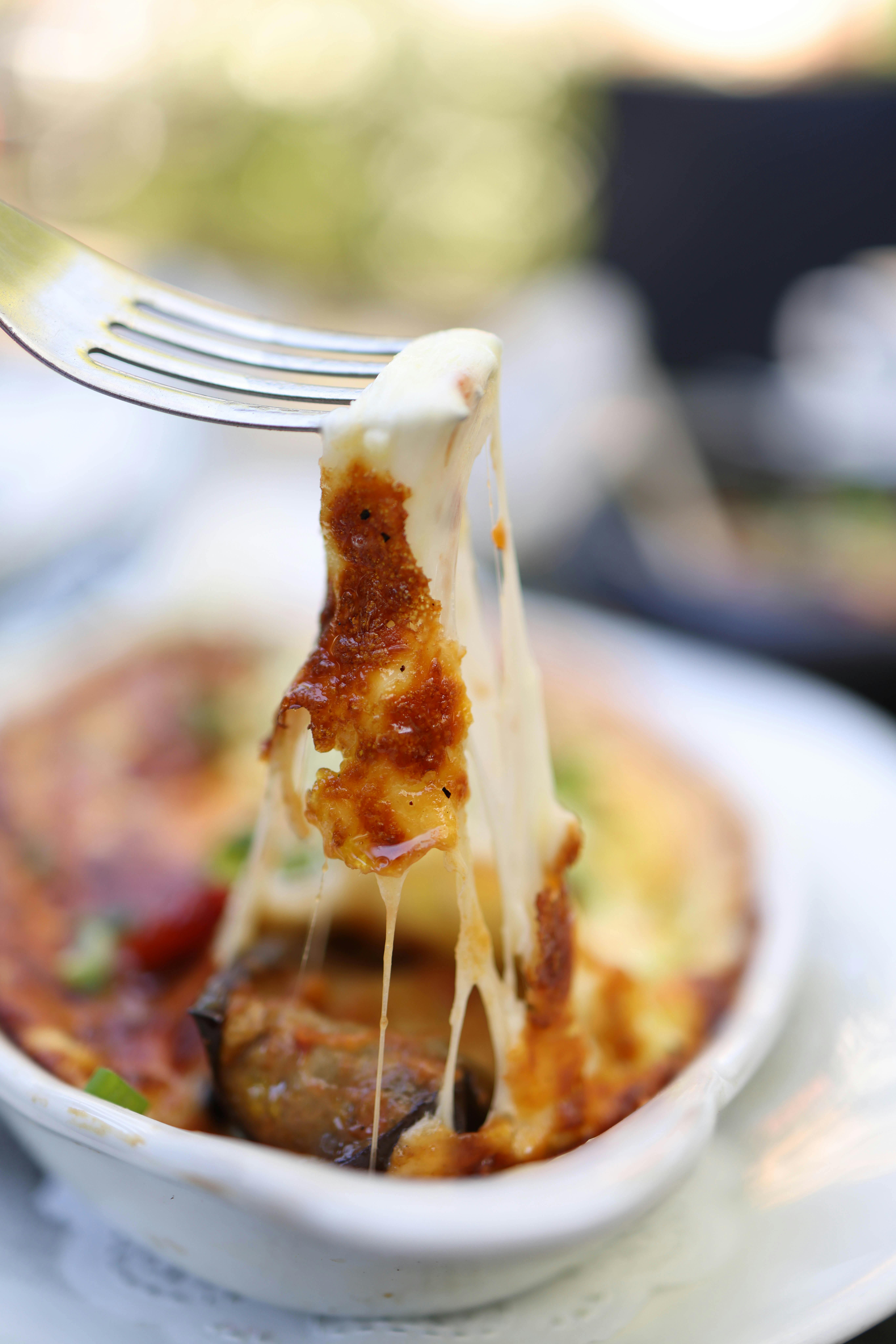 Indulgent baked cheese dish close-up with fork showing melted cheese, perfect for food lovers.