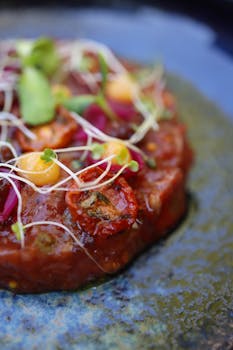 A close-up of a vibrant vegetable tartare garnished with fresh microgreens and sauces.