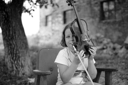 A young child poses outdoors holding a violin, captured in black and white.