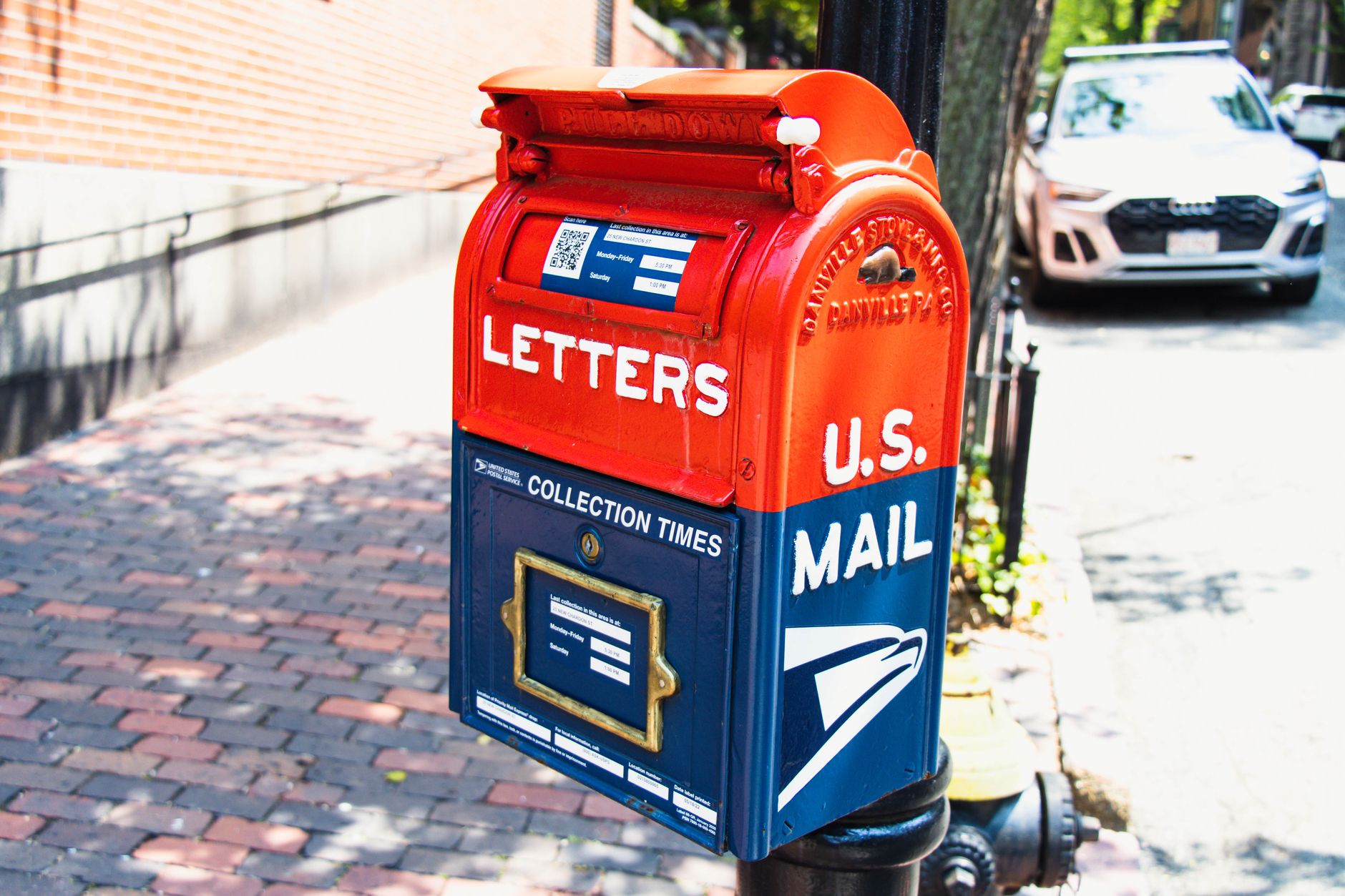 Vibrant U.S. mailbox on a city sidewalk with a parked car, conveying a classic urban scene.