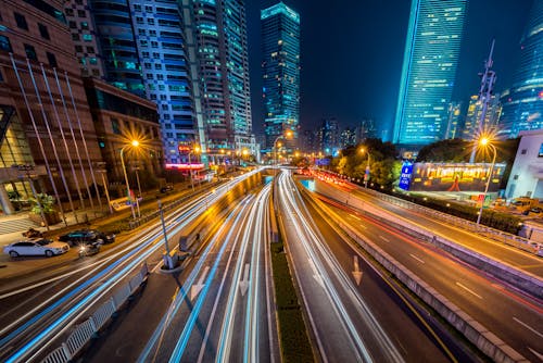 Timelapse Fotografii Pojazdu Na Betonowej Drodze W Pobliżu Budynku Wysokiego Wzrostu W Nocy