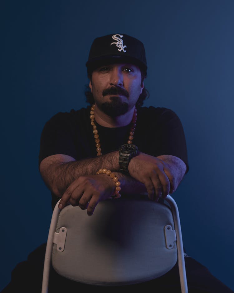 Hairy Man In Black Baseball Cap Sitting Backwards On Chair