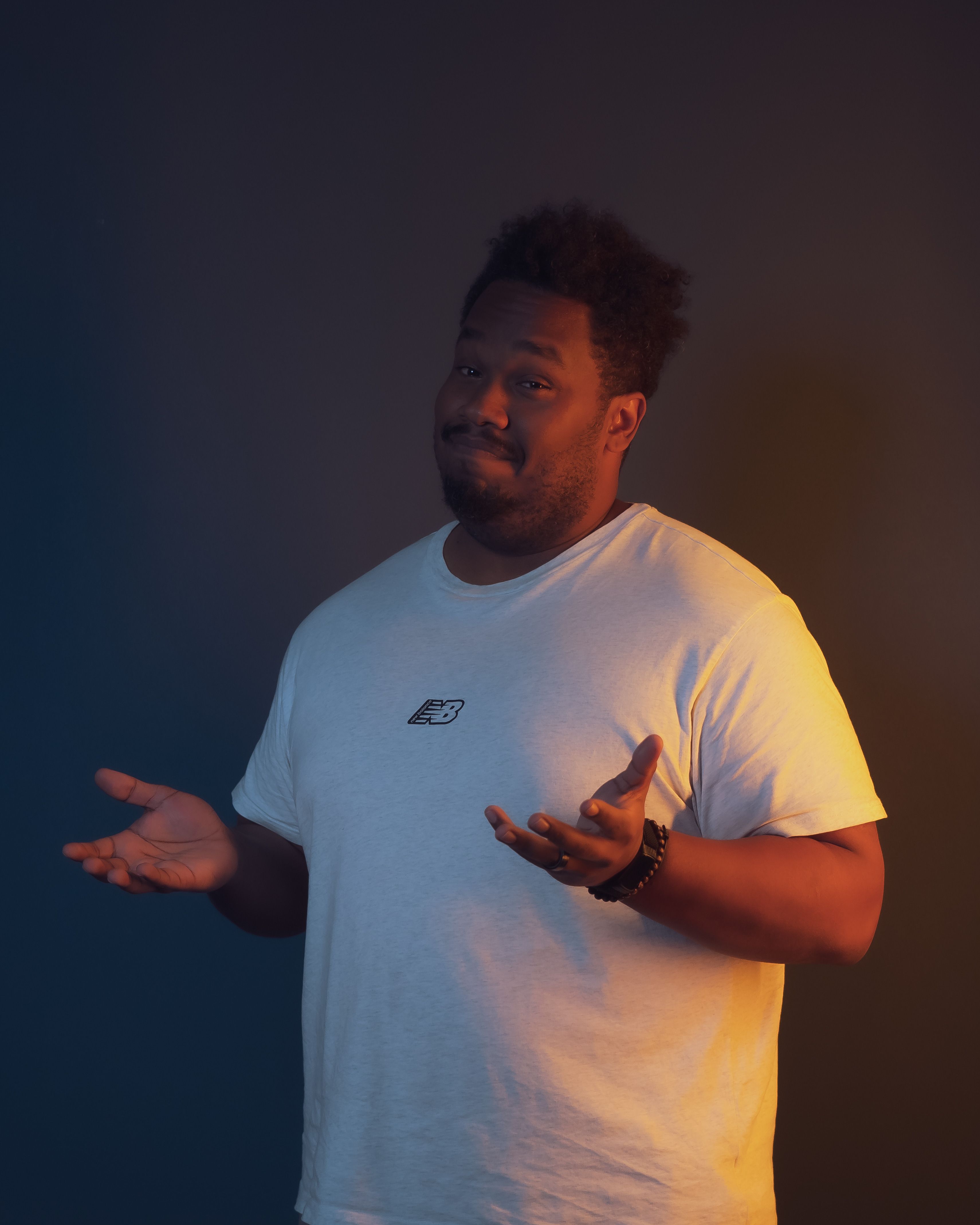 Portrait of a man standing with a confident pose in a white t-shirt against a dark background.