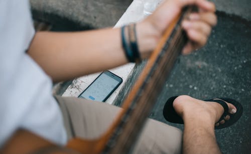 Person Holding Guitar Sitting Beside Black Smartphone