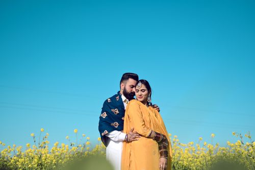 Free A couple in traditional Indian attire embracing amid a vibrant floral field under a clear blue sky. Stock Photo