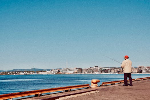 A man fishing on a pier in Oslo with a stunning urban cityscape backdrop under a clear blue sky.