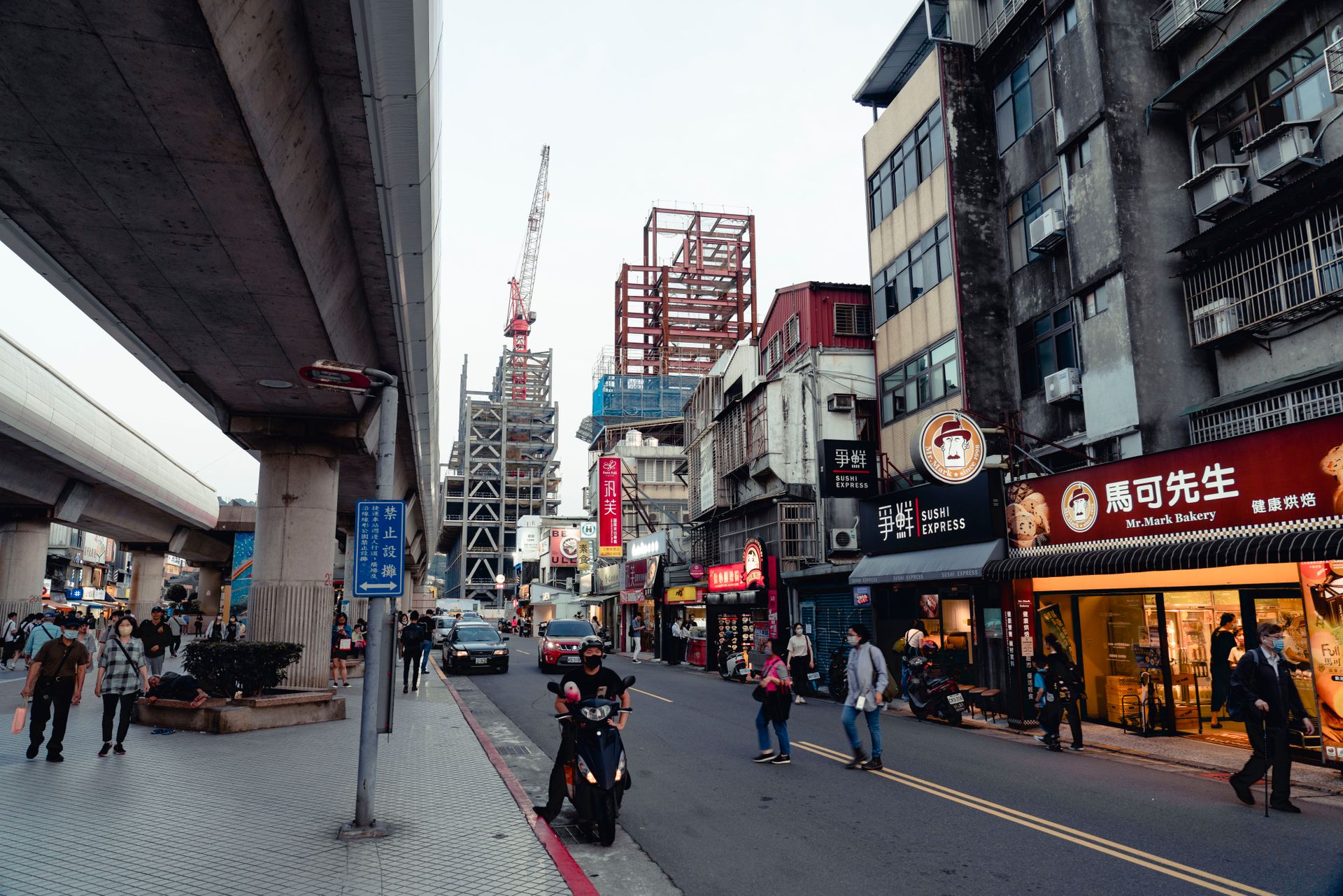 A bustling city street with shops, construction, and diverse pedestrians in an Asian metropolis.
