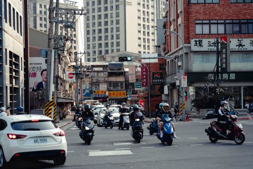 Free Dynamic city street scene featuring motor scooters and cars in an urban intersection. Stock Photo
