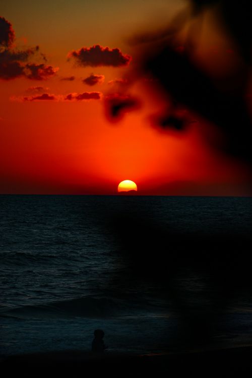 Free Captivating sunset over the ocean with red and orange sky hues, silhouetting waves and clouds. Stock Photo