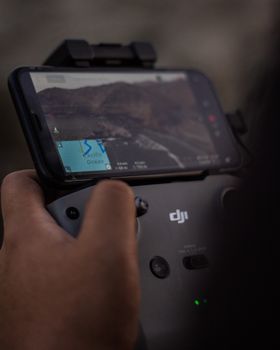 Close-up of a person using a smartphone to control a drone, displaying a map on the screen.