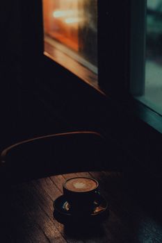 A warm and cozy scene of a coffee cup on a wooden table near a window, capturing a tranquil dawn atmosphere.