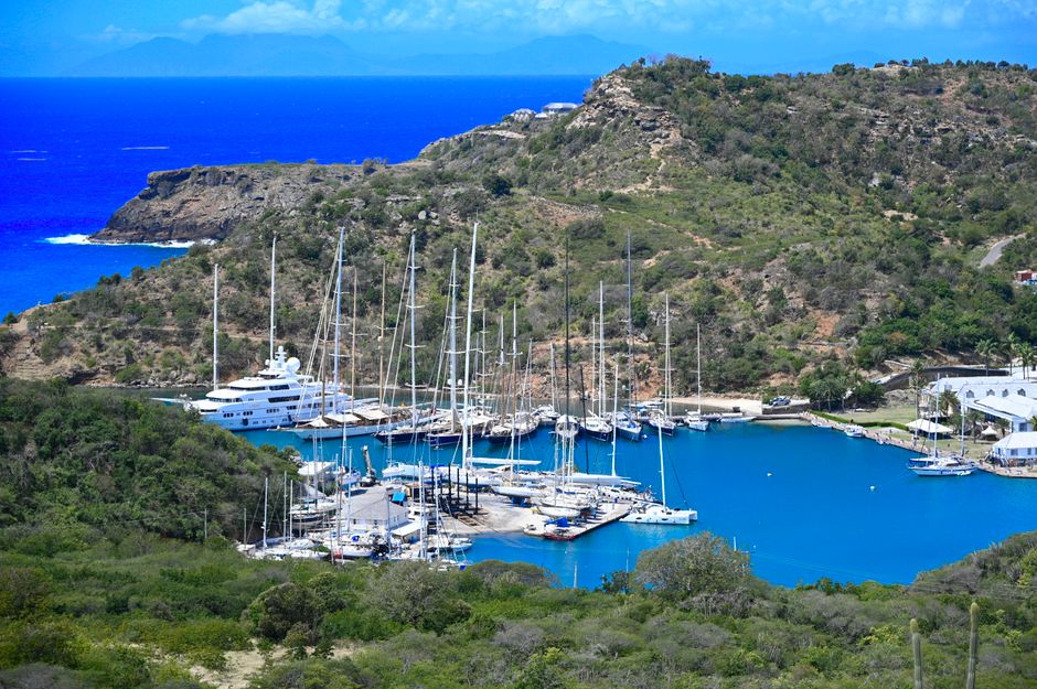 Stunning aerial view of a serene harbor with moored yachts, surrounded by lush hills and vibrant blue water.