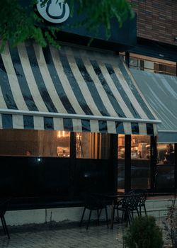 A quaint café with a striped awning on a rainy evening, capturing urban tranquility.