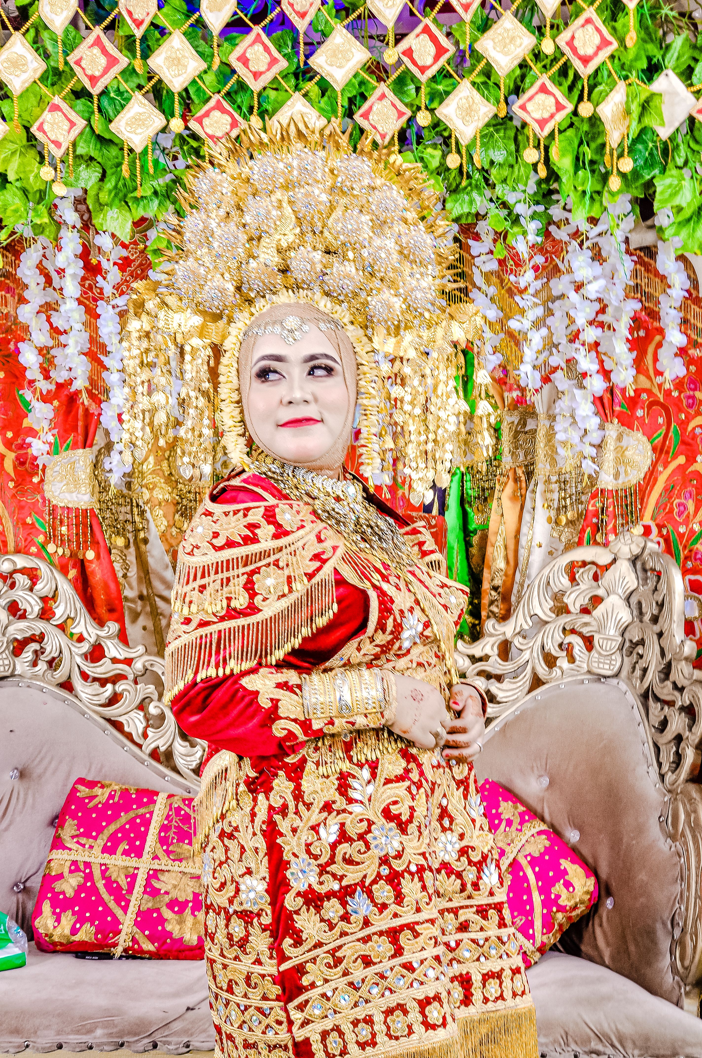 A beautiful bride in intricate gold and red traditional attire posing elegantly indoors.