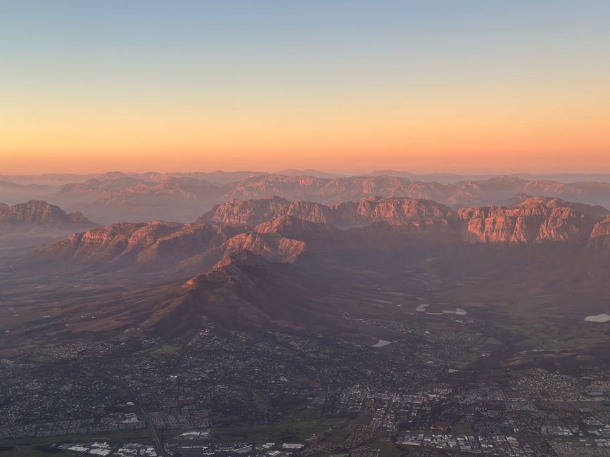 Outstanding Helicopter, Quad Bike, & Champagne Sunset Cruise in Cape Town Review Review 2026 - Breathtaking aerial view of rocky mountains with glowing sunset hues and distant cityscape below.