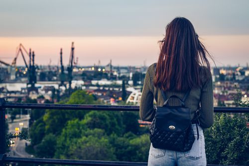 Free Woman with backpack gazing at Gdańsk's industrial skyline at sunset reflecting urban exploration. Stock Photo