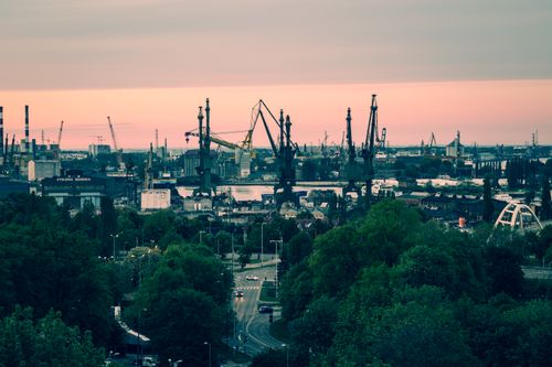 Free A panoramic view of the iconic Gdańsk shipyard with cranes silhouetted against a vibrant sunset sky. Stock Photo