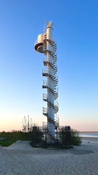Scenic view of a spiral navigation tower on a sandy beach in Świnoujście, Poland at sunset.