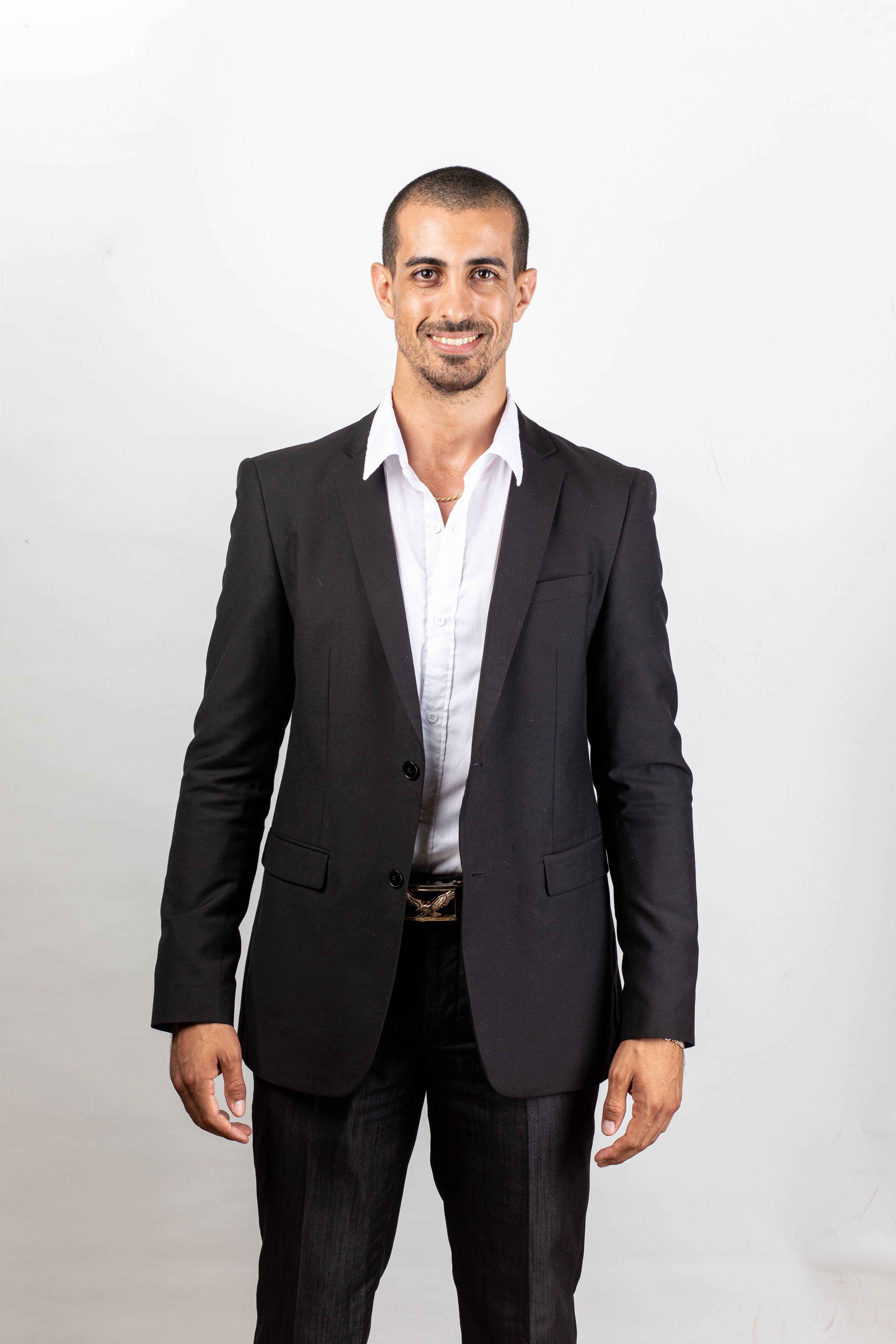 Portrait of a confident businessman in a black suit, smiling against a neutral background.