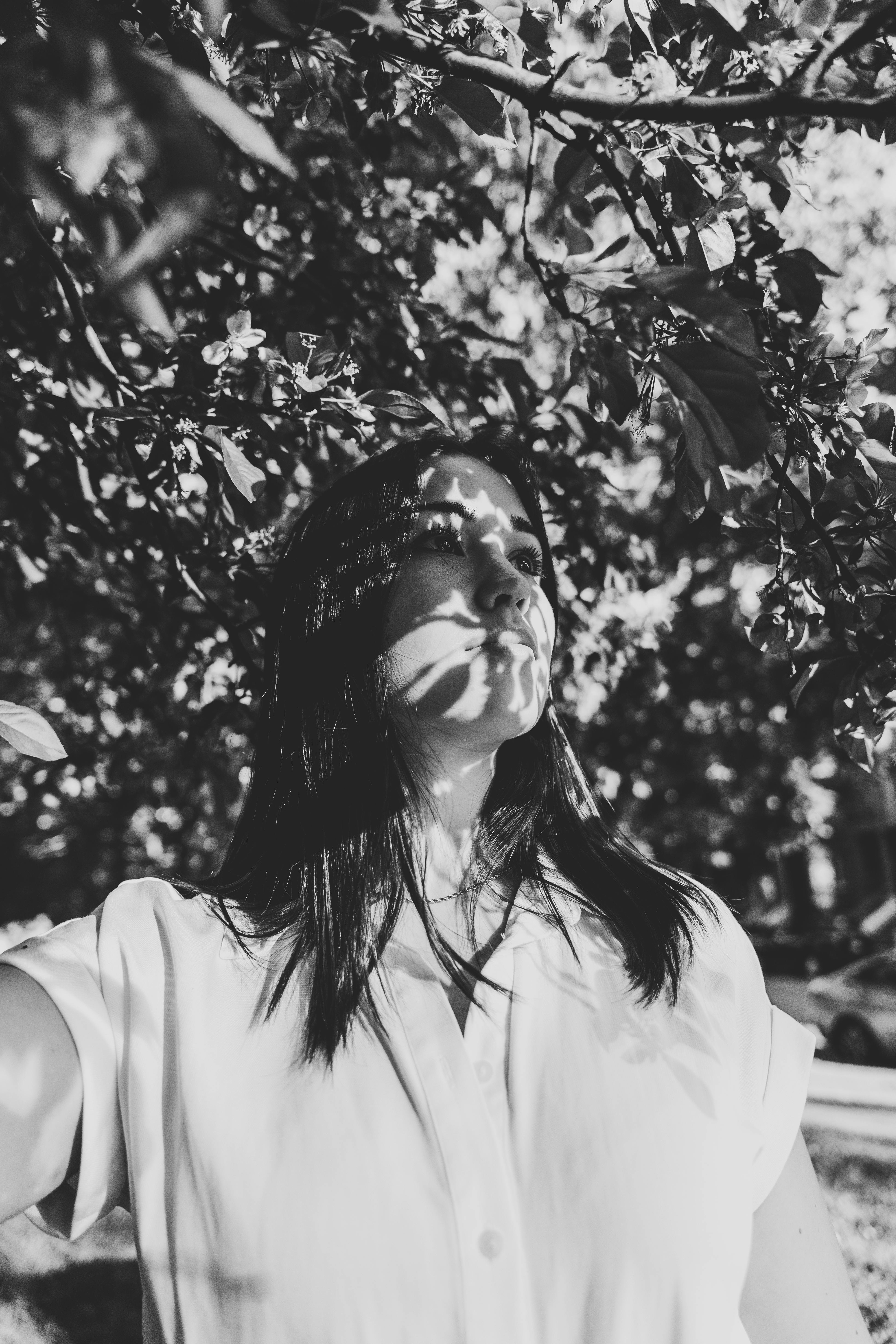 Black and white portrait of a woman under tree shadows, creating a delicate natural pattern.