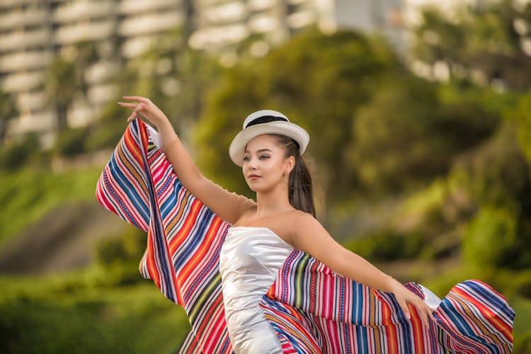 Young Woman In A Patterned Dress And Hat Posing Outside 