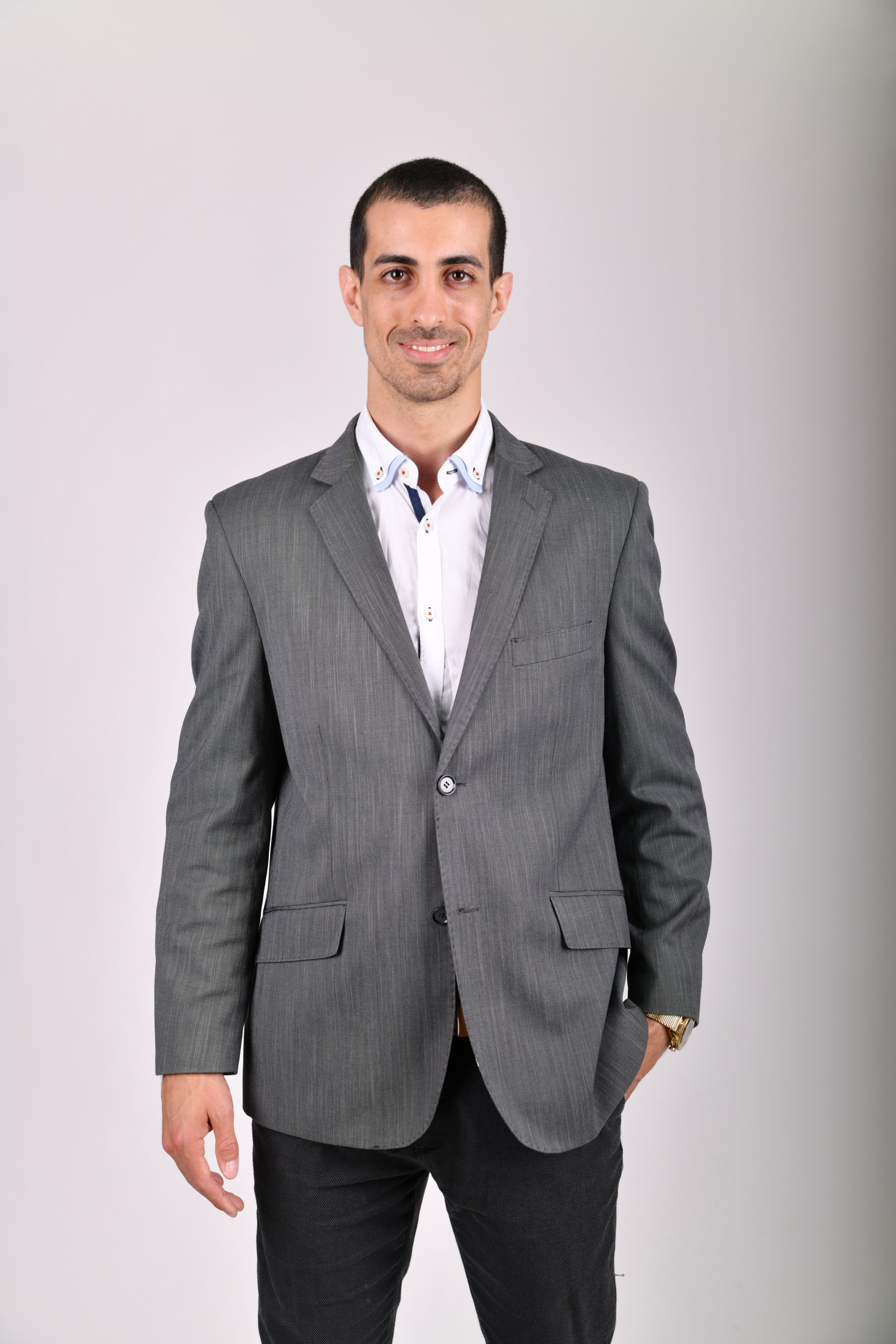 A well-dressed man in a gray jacket smiling in a studio shoot.