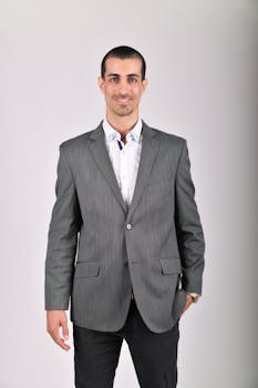 A well-dressed man in a gray jacket smiling in a studio shoot.