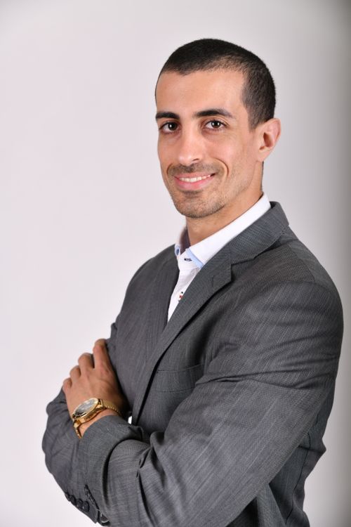 Free Portrait of a confident man in a gray suit with arms crossed, smiling in a studio setting. Stock Photo