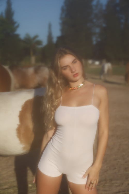 Woman in White Summer Bodysuit Posing against Horses