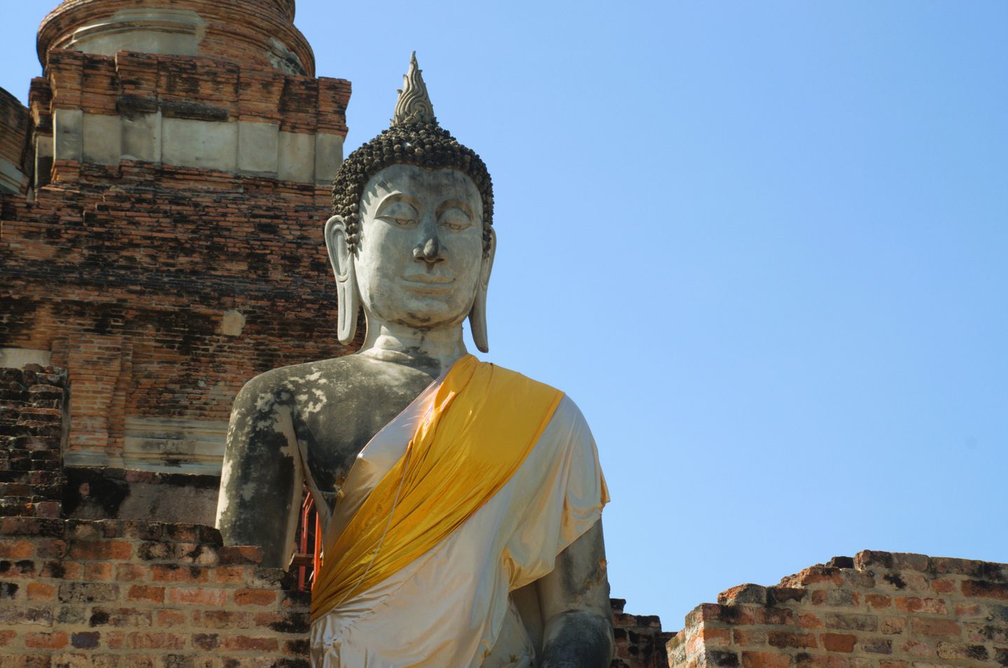 Een serene Boeddha-standbeeld tegen een oud bakstenen tempel en heldere blauwe lucht.