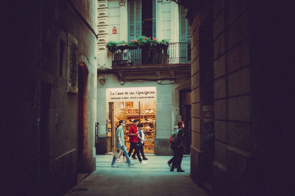 Personas caminando por un callejón con vista a la fachada de una tienda en un entorno urbano histórico.