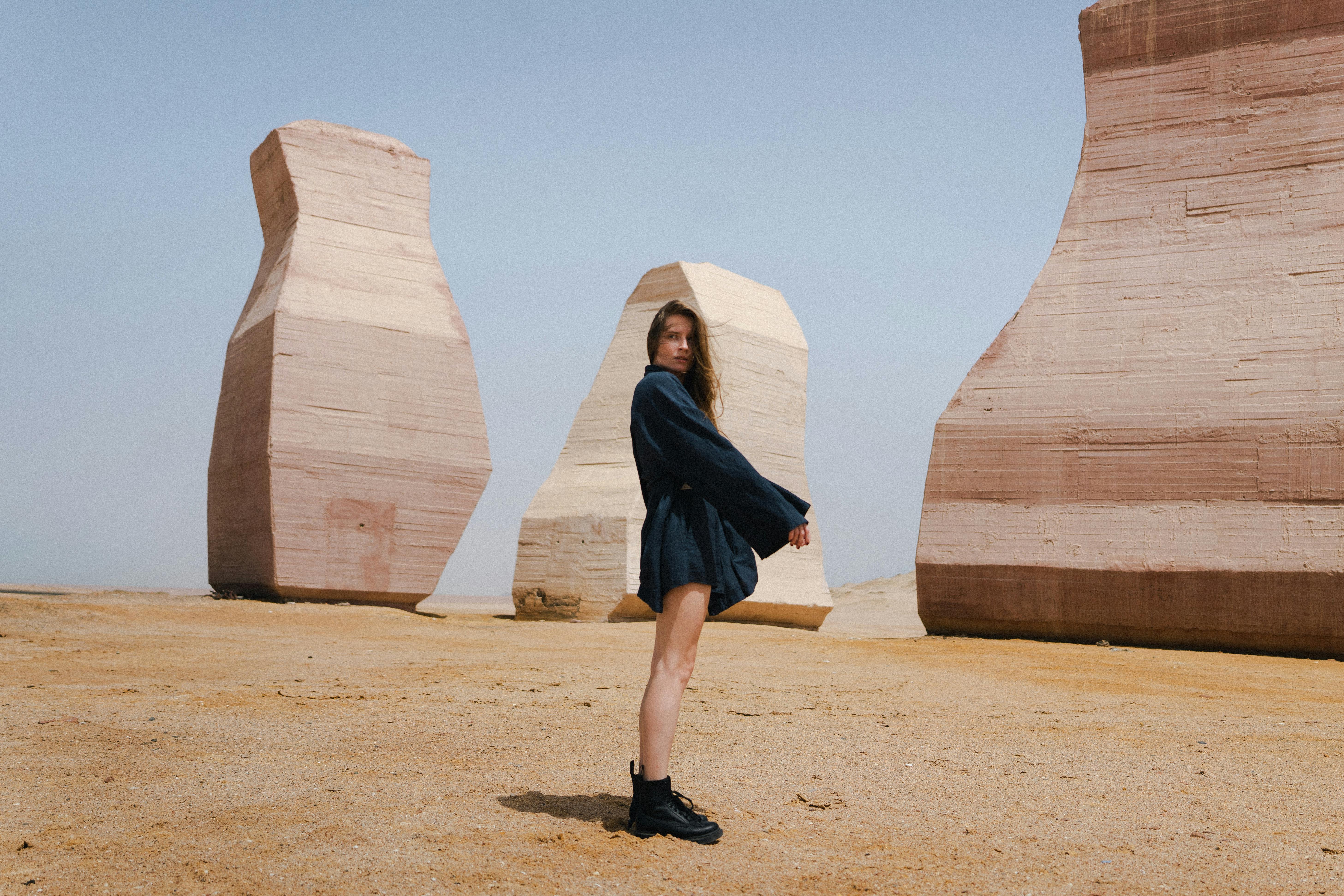 A young woman posing among unique stone sculptures in an Egyptian desert setting.
